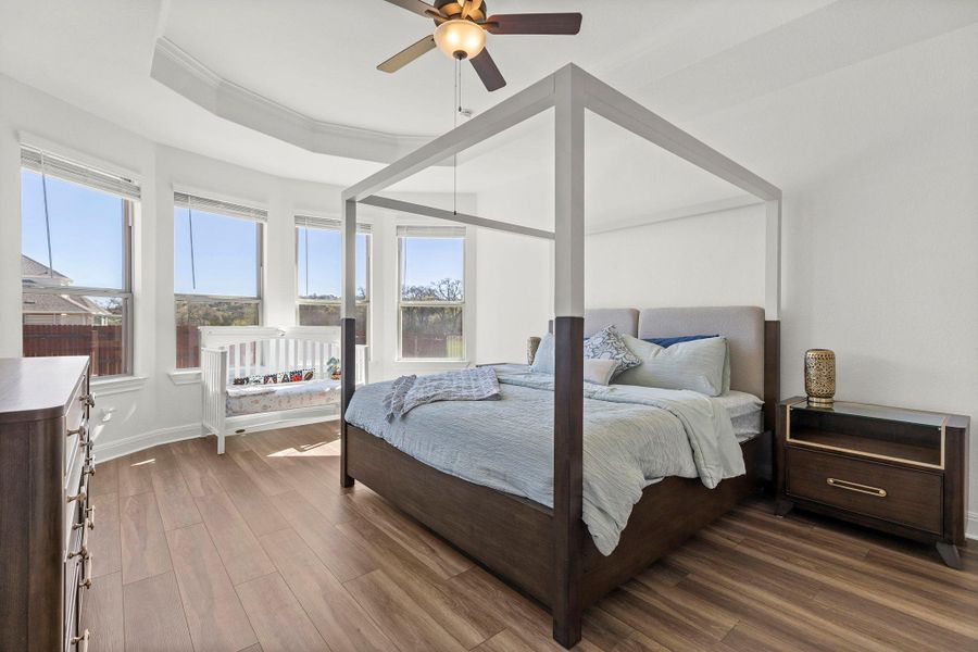 Bedroom featuring dark wood-style flooring, a ceiling fan, ornamental molding, and a raised ceiling