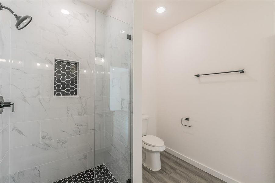 Full bathroom featuring wood finished floors, a marble finish shower, toilet, and baseboards