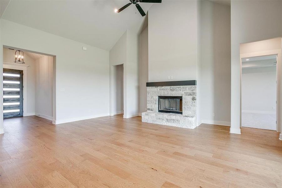 Unfurnished living room with ceiling fan with notable chandelier, high vaulted ceiling, light hardwood / wood-style flooring, and a fireplace