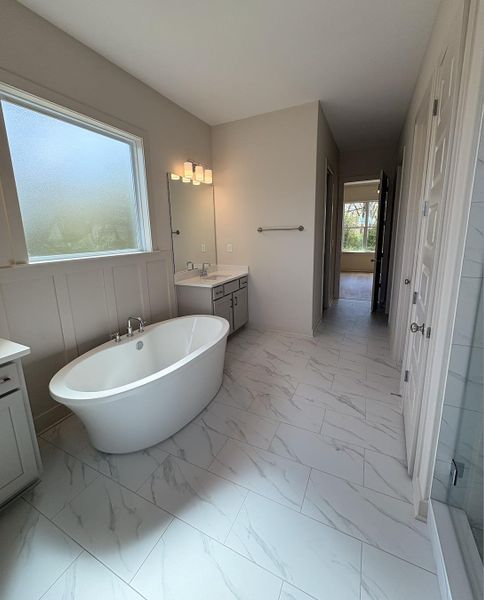 Full bath with vanity, a soaking tub, and light marble finish floors