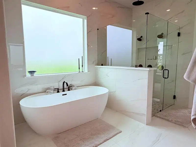 Freestanding soaking tub with a matte black faucet fixture, set against large format white tile walls featuring subtle veining