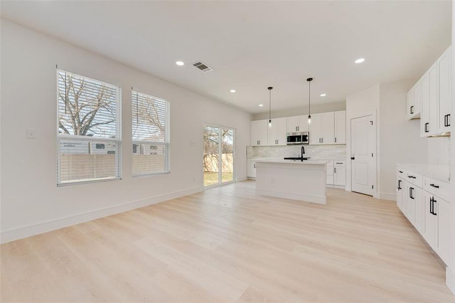 Kitchen with a kitchen island with sink, hanging light fixtures, light hardwood / wood-style flooring, a wealth of natural light, and white cabinetry