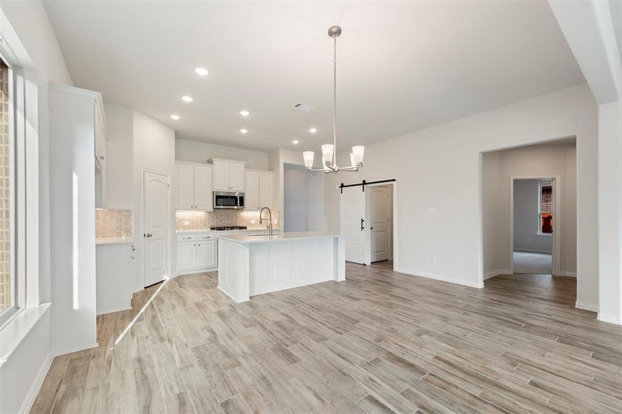 Kitchen with a barn door, hanging light fixtures, white cabinetry, decorative backsplash, and recessed lighting