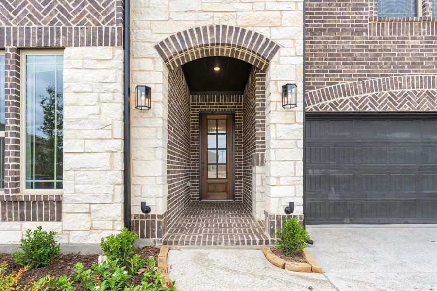 Home entrance with stone archway, dark brick, wood front door, and wall sconce lighting Home entrance with stone archway, dark brick, wood front door, and wall sconce lighting