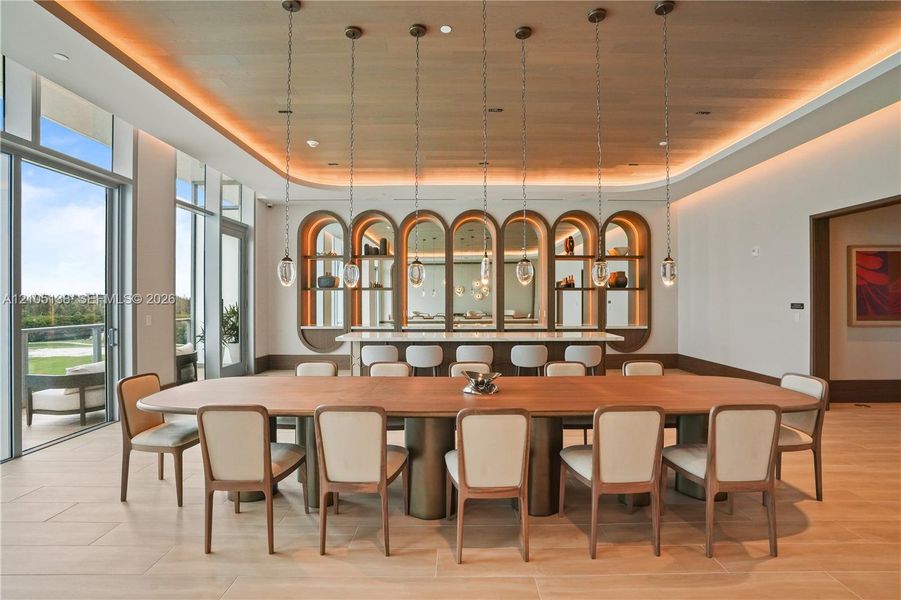 Open-concept dining area featuring a long wood dining table, recessed ceiling lighting, a built-in bar with arched shelving and mirrored accents, and full-height glass doors