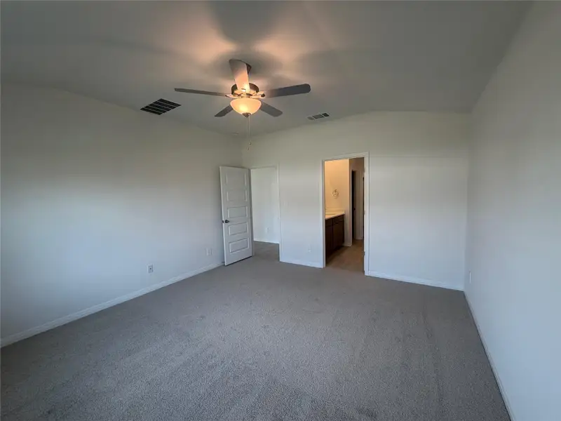 Unfurnished bedroom featuring light colored carpet, lofted ceiling, a ceiling fan, and connected bathroom