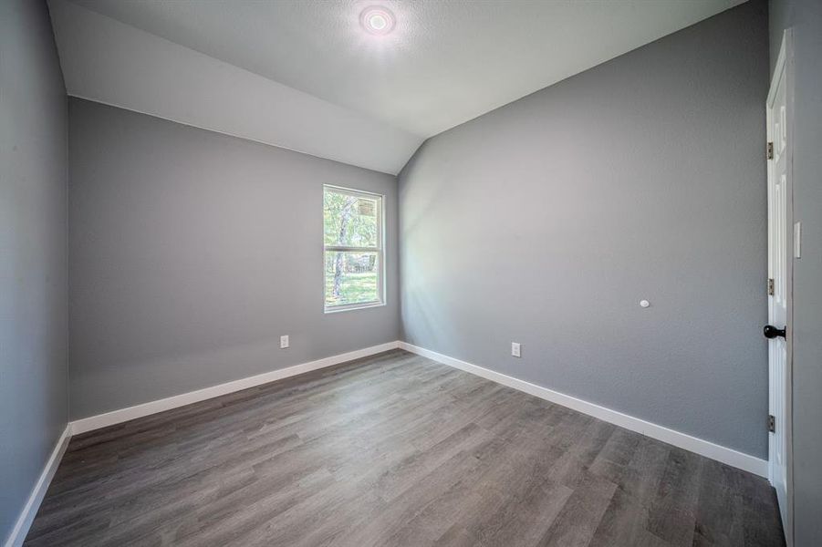 Unfurnished room with vaulted ceiling and dark wood-style flooring Unfurnished room with vaulted ceiling and dark wood-style flooring