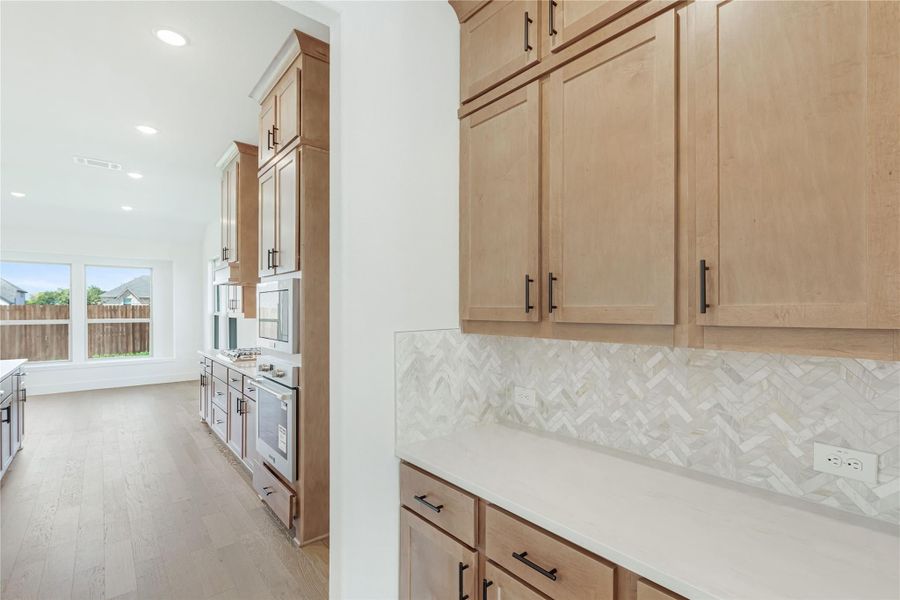 Kitchen with light wood cabinets, herringbone tile backsplash, white countertops, and hardwood floors