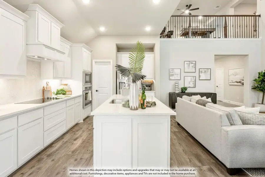 Open-concept kitchen with white cabinets, center island, and wood floors flowing into living area with second-floor loft above