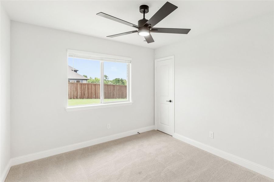 Empty bedroom with carpet flooring, ceiling fan, and window overlooking backyard fence