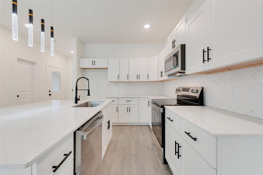 Kitchen with white cabinets, stainless steel appliances, a sink, and decorative light fixtures