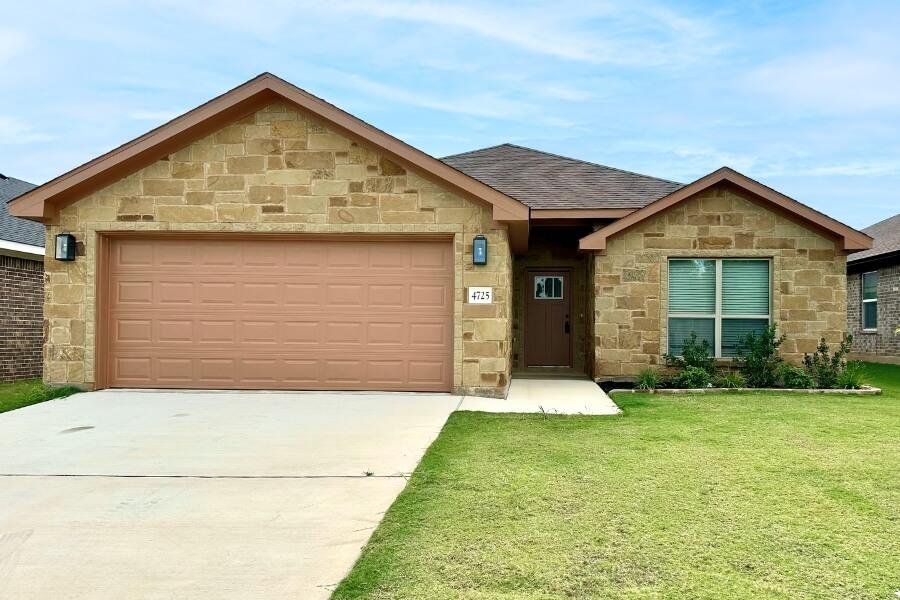 View of front of property featuring stone siding, concrete driveway, a shingled roof, a front yard, and an attached garage