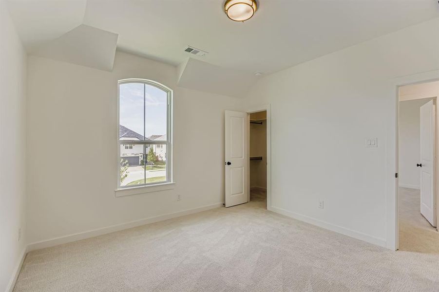 Unfurnished bedroom featuring light colored carpet, lofted ceiling, and a walk in closet