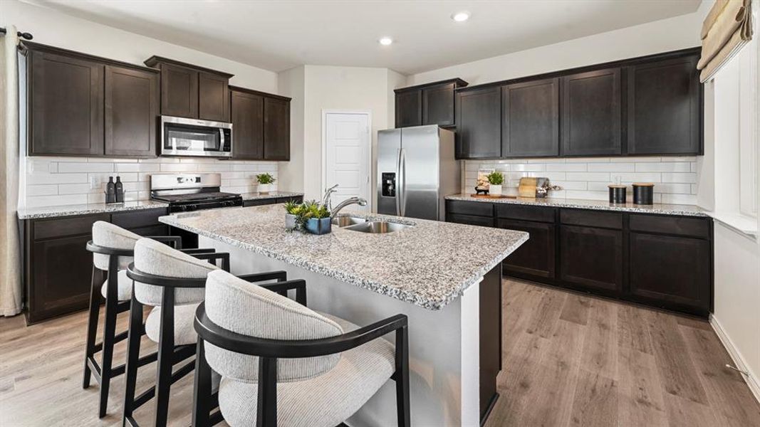 Kitchen with stainless steel appliances, decorative backsplash, light wood-style floors, light stone counters, and dark brown cabinets Kitchen with stainless steel appliances, decorative backsplash, light wood-style floors, light stone counters, and dark brown cabinets