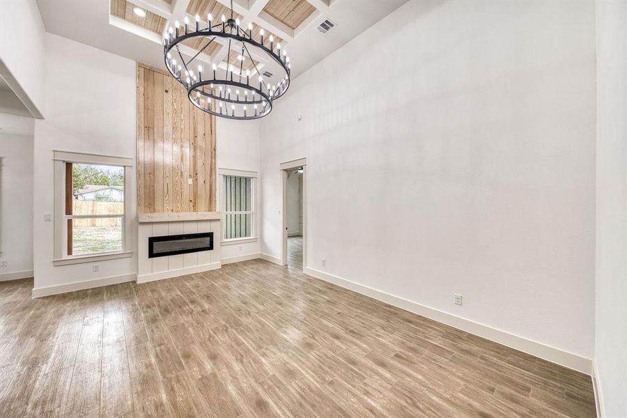 Unfurnished living room featuring coffered ceiling, light wood finished floors, hanging lights, and a tiled fireplace