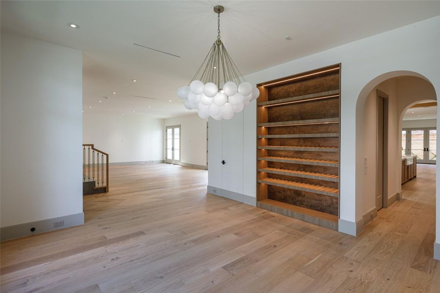 The rooms connect without losing their identities. Arched openings, white oak floors, a glowing wine display, and a sculptural chandelier create an easy progression from dining to living to kitchen in this newly completed home.