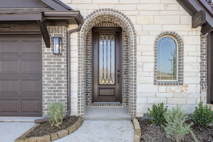 Home entrance with arched brick doorway, dark wood and iron front door, stone exterior, and attached garage