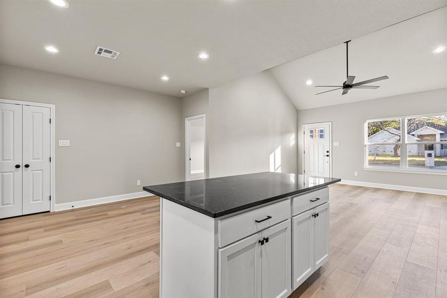 Kitchen featuring recessed lighting, vaulted ceiling, white cabinetry, light wood-style floors, and a kitchen island Kitchen featuring recessed lighting, vaulted ceiling, white cabinetry, light wood-style floors, and a kitchen island