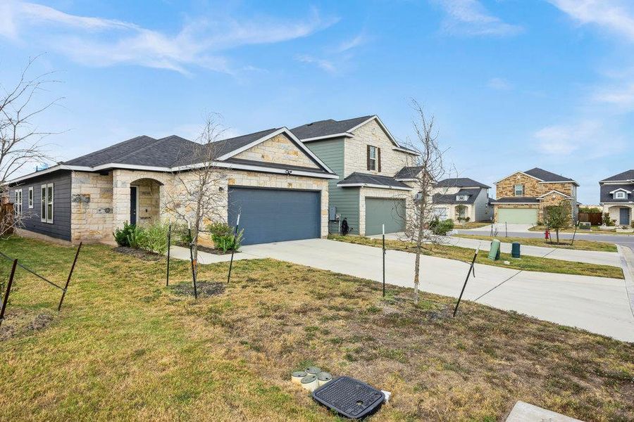 View of front facade featuring stone siding, concrete driveway, and a front yard