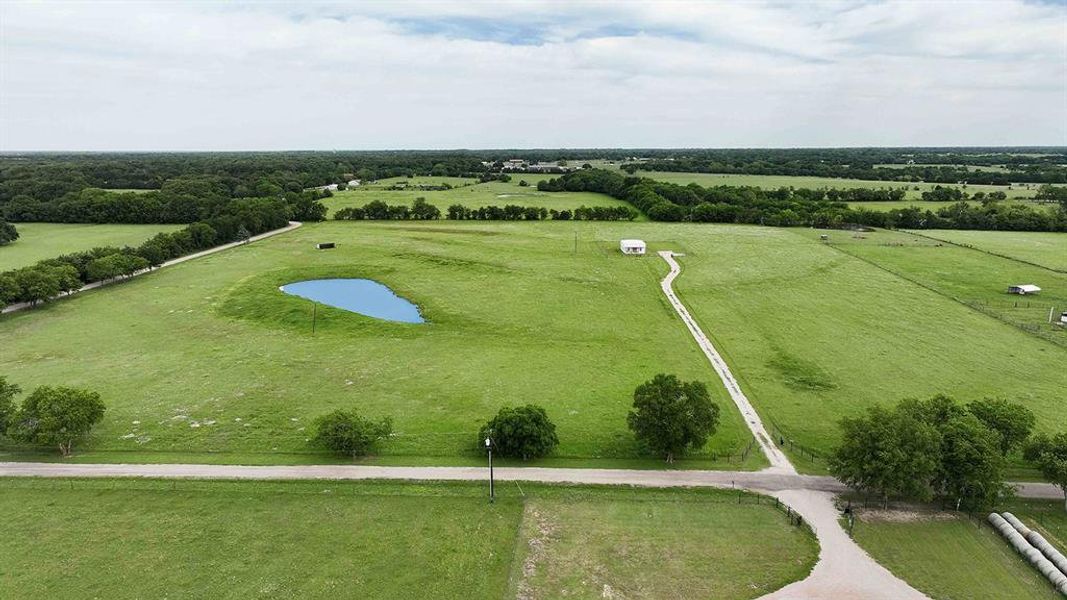Expansive green acreage featuring a serene pond, a winding gravel driveway, and a small white structure