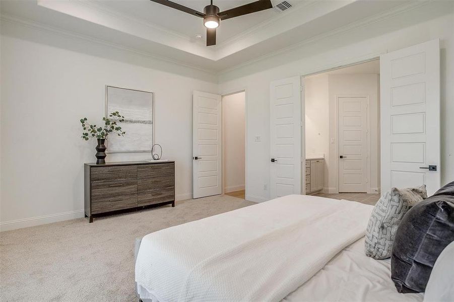 Primary bedroom featuring ensuite bath, a raised ceiling, and ceiling fan