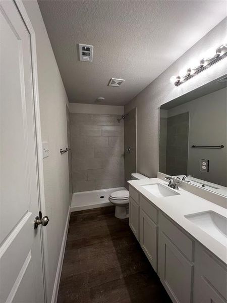 Bathroom with hardwood / wood-style floors, vanity, toilet, tiled shower, and a textured ceiling