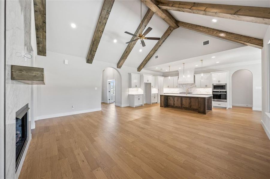 Unfurnished living room with arched walkways, a fireplace, ceiling fan, recessed lighting, and light wood-style floors
