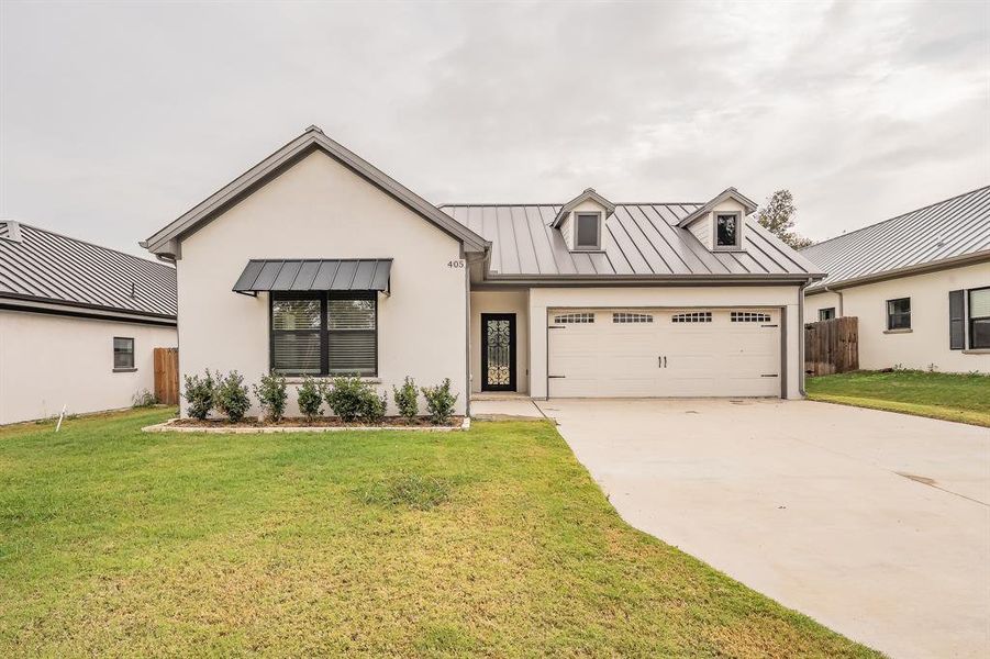 Modern inspired farmhouse featuring a standing seam roof, a metal roof, concrete driveway, and stucco siding Modern inspired farmhouse featuring a standing seam roof, a metal roof, concrete driveway, and stucco siding