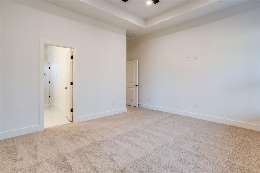 Unfurnished bedroom with light colored carpet, ensuite bathroom, a tray ceiling, and a ceiling fan