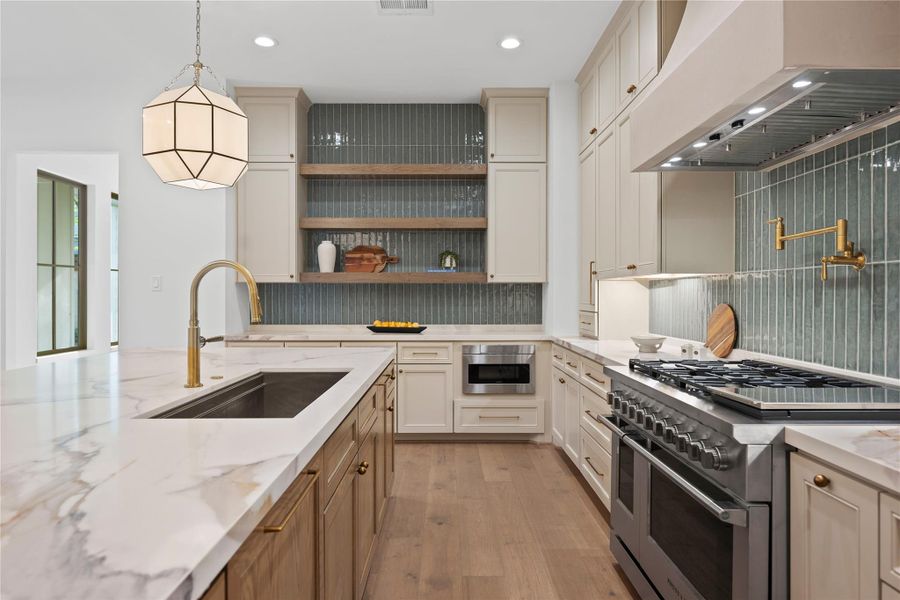 Two-toned cabinetry paired with subtle sage tone backsplash. Wooden shelves provided for additional storage and create an open, are feel, enhancing space with both function and style. Two-toned cabinetry paired with subtle sage tone backsplash. Wooden shelves provided for additional storage and create an open, are feel, enhancing space with both function and style.