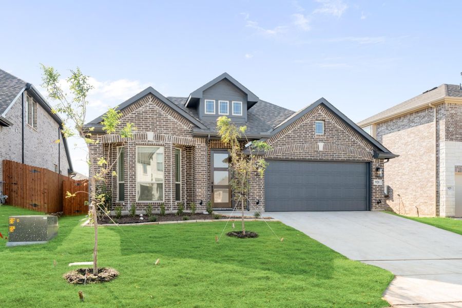 Two-story brick home with gray two-car garage, large windows, and green front lawn with young trees. Two-story brick home with gray two-car garage, large windows, and green front lawn with young trees.