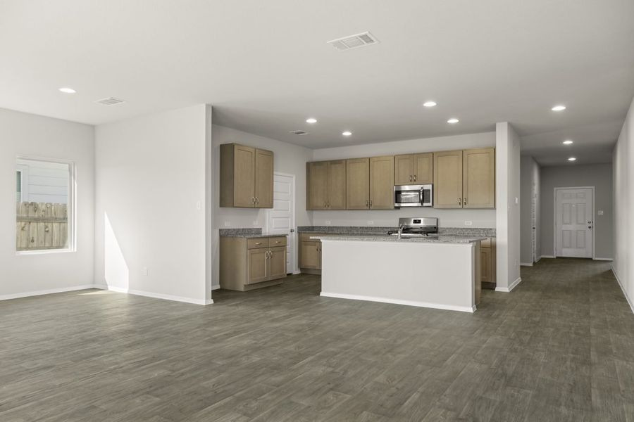Image of home kitchen with light brown cabinets, center island, wood-look floors and white walls. Dining room on the left and entry way to front door on the right