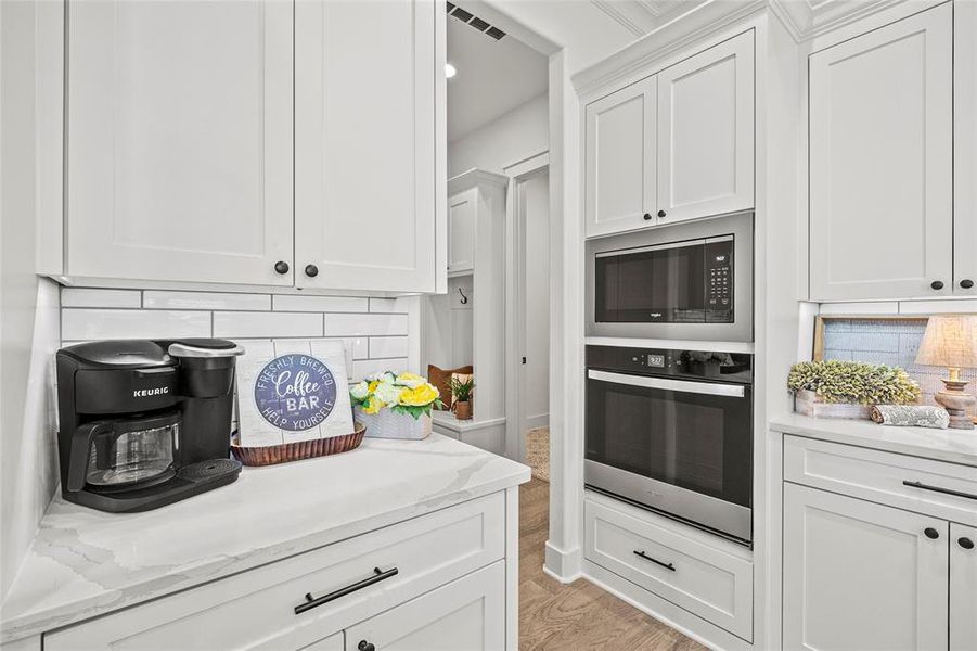 Kitchen featuring light hardwood / wood-style flooring, white cabinets, black microwave, tasteful backsplash, and stainless steel oven