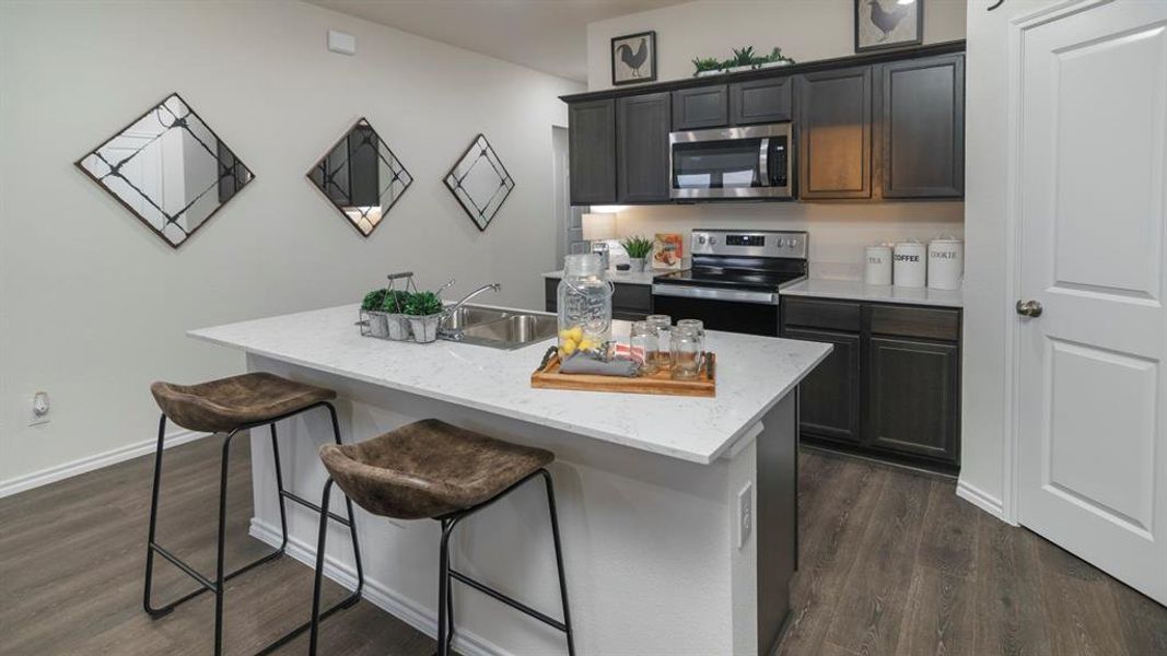 Kitchen featuring a breakfast bar area, stainless steel appliances, dark wood finished floors, a center island with sink, and light stone counters