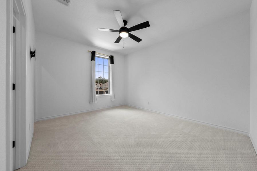 Comfortable bedroom with neutral tones, plush carpeting, and a modern ceiling fan.