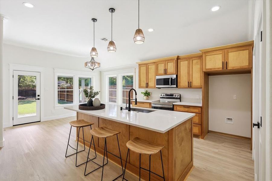 Kitchen featuring light wood-style floors, appliances with stainless steel finishes, pendant lighting, a breakfast bar, and recessed lighting