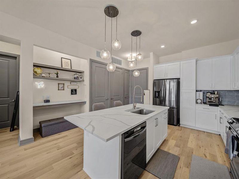 Kitchen with pendant lighting, light wood-style floors, appliances with stainless steel finishes, a kitchen island with sink, and tasteful backsplash Kitchen with pendant lighting, light wood-style floors, appliances with stainless steel finishes, a kitchen island with sink, and tasteful backsplash
