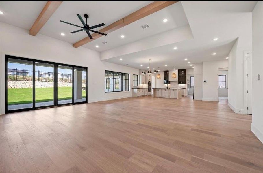 living room with a wealth of natural light, light hardwood / wood-style flooring, beamed ceiling, and ceiling fan with notable chandelier