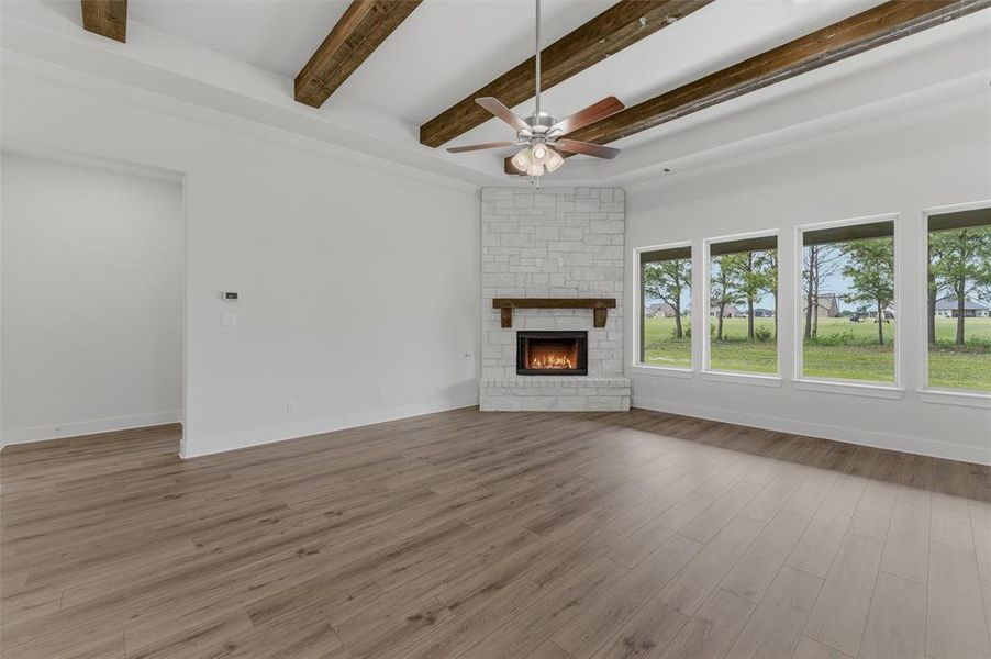 Spacious living area featuring a stone-clad fireplace with a wood mantel, wood-finish flooring, and exposed wood ceiling beams