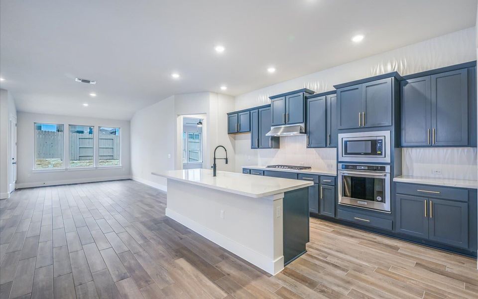 Kitchen featuring stainless steel appliances, a center island with sink, wood tiled floors, open floor plan, and recessed lighting