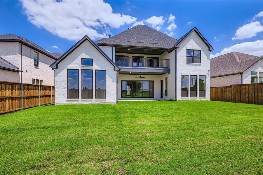 Back of house featuring a balcony, a ceiling fan, a fenced backyard, and brick siding