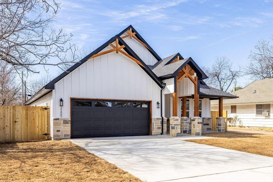 Modern inspired farmhouse featuring driveway, stone siding, roof with shingles, an attached garage, and fence