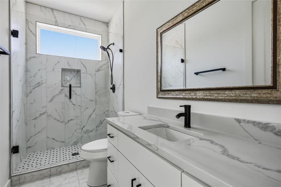 A well-lit bathroom features a spacious vanity with sleek countertops and a walk-in shower with elegant tile work.