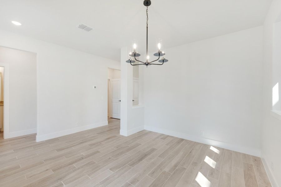 Empty dining room with light wood-look tile floors, white walls, and a black five-arm chandelier overhead.