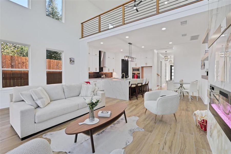 Living room featuring plenty of natural light, a towering ceiling, light wood-style flooring, and a chandelier