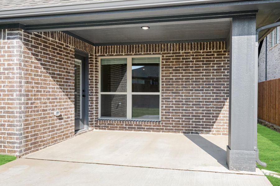 Covered back patio with concrete slab, brick exterior wall, and a large window with gray door. Covered back patio with concrete slab, brick exterior wall, and a large window with gray door.
