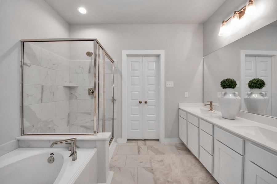 Escape to a spa-like oasis in this primary bathroom. Enjoy a walk-in shower with tile surround, a separate garden tub with custom detailing, and an elegant vanity featuring light countertops, modern hardware, and beautiful vanity lights. Experience luxury and relaxation in every detail. Sample photo of completed home with similar floor plan. Actual colors and selections may vary.