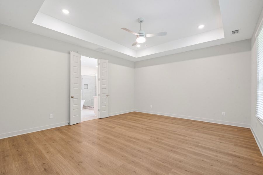 Spacious room featuring wood-finish flooring, a tray ceiling with recessed lighting, and a ceiling fan Spacious room featuring wood-finish flooring, a tray ceiling with recessed lighting, and a ceiling fan