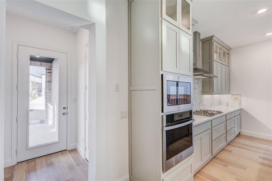 Kitchen featuring wall chimney range hood, decorative backsplash, light hardwood / wood-style floors, and appliances with stainless steel finishes