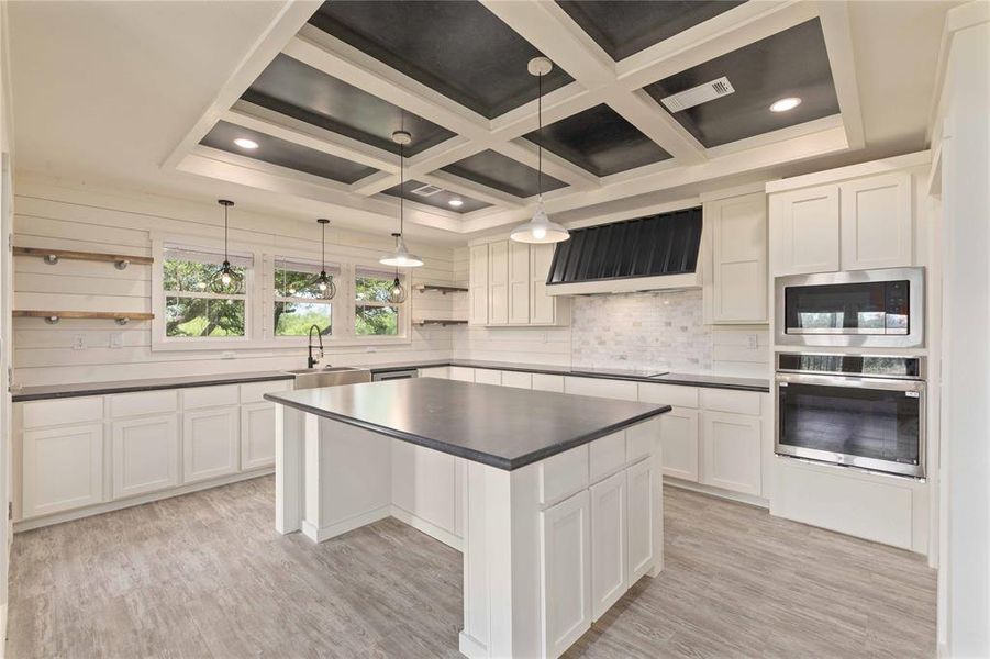 Open-concept kitchen featuring a coffered ceiling, a central island, stainless steel built-in appliances, white shaker cabinetry, and wood-finish flooring